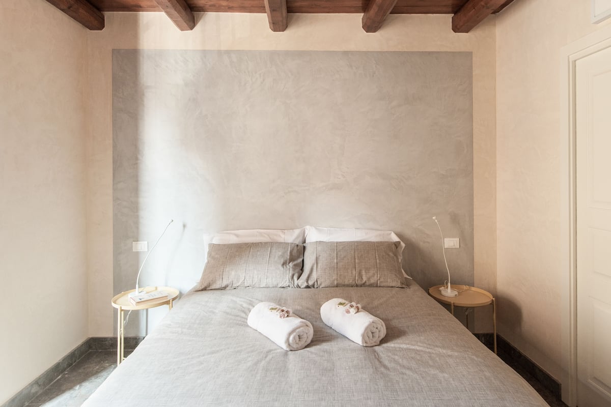 Quarto minimalista com uma cama grande, duas mesas de cabeceira e uma paleta de cores neutras.