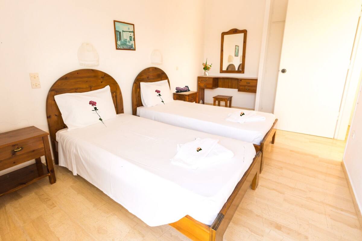 A hotel room with two single beds, a wooden dresser, a bedside table, a mirror, and a door.