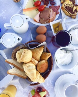 Ein Frühstückstisch mit Brot, Eiern, Schinken, Käse, Tomaten und einer Tasse Kaffee.