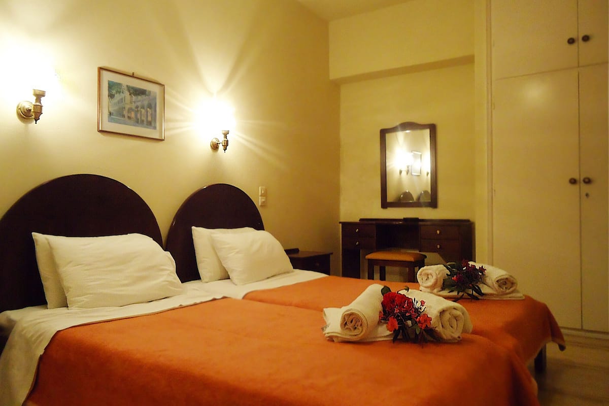 A hotel room with two beds, a desk, a mirror, and a wardrobe.