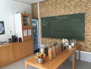 A breakfast area with a chalkboard menu, a coffee machine, and various food items on a table. - Hestkær Family Rooms (Grindsted)