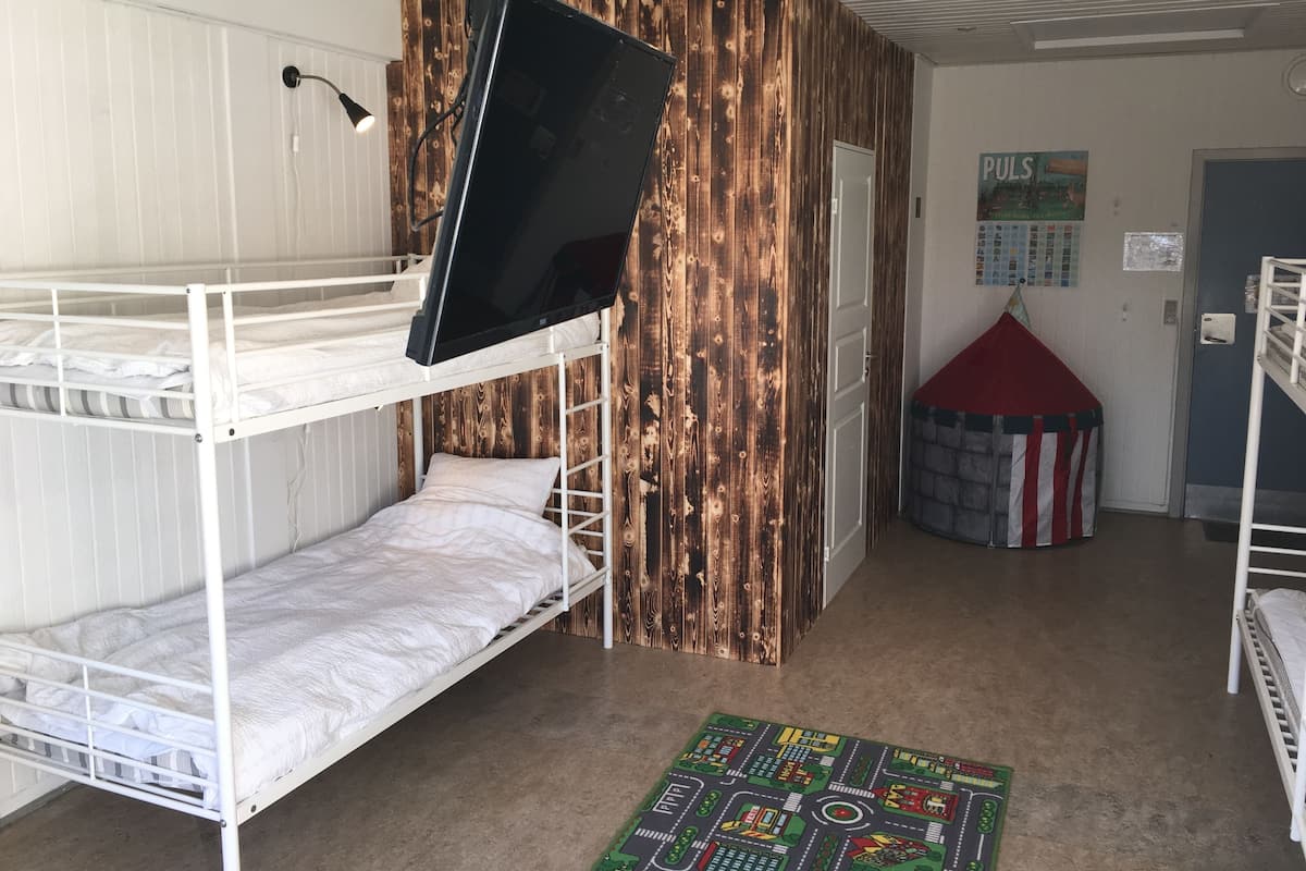 A bunk bed room with a television mounted on the wall, a wooden accent wall, a small play tent, and a colorful play mat on the floor.