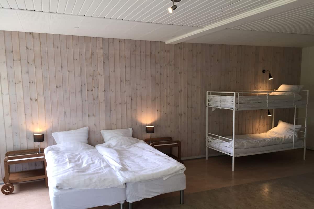 A room with a bunk bed, a double bed, and a wooden wall. There are two bedside tables with lamps.