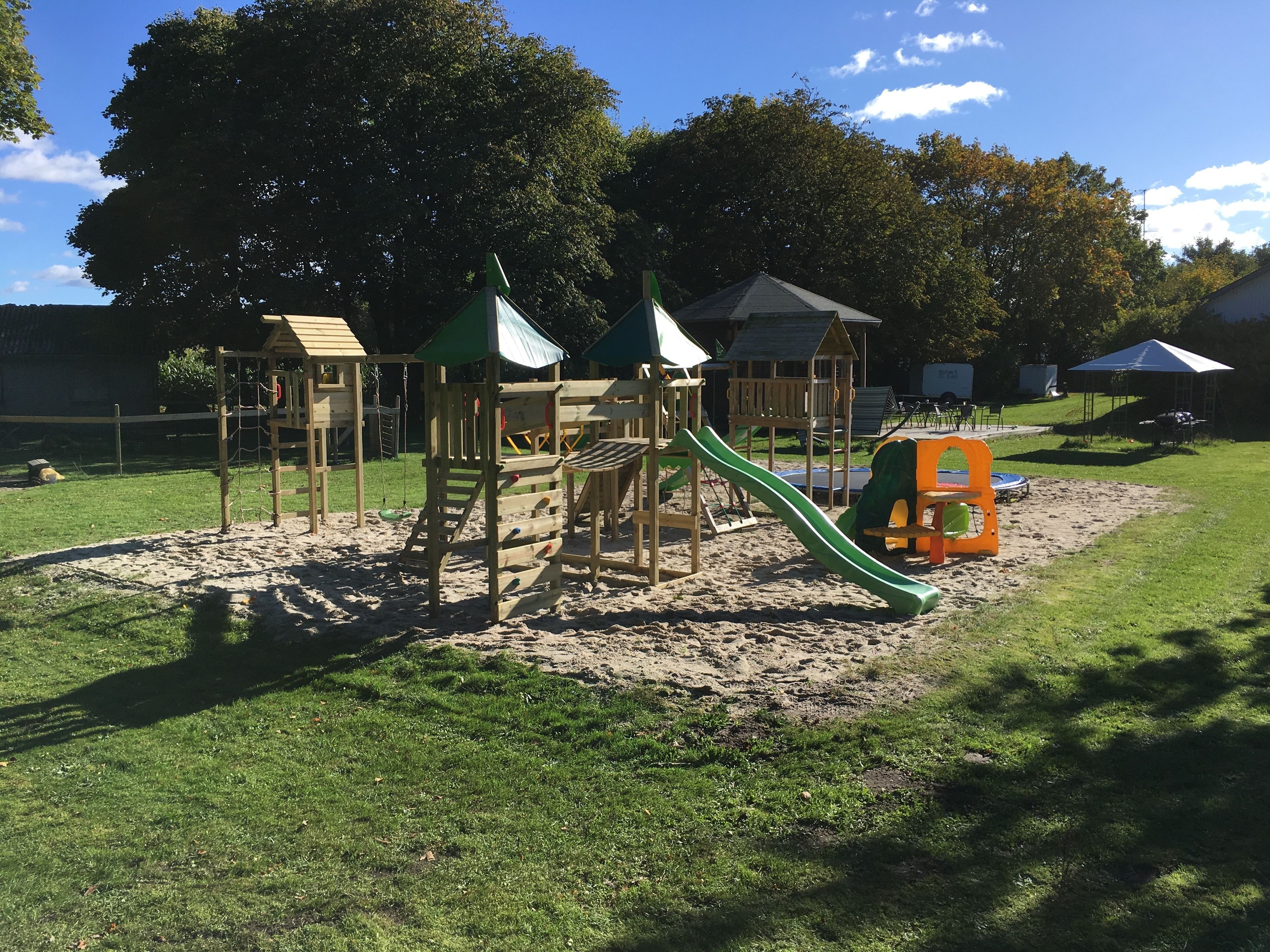 A playground with various play structures, including slides and climbing areas, surrounded by sand and grass.