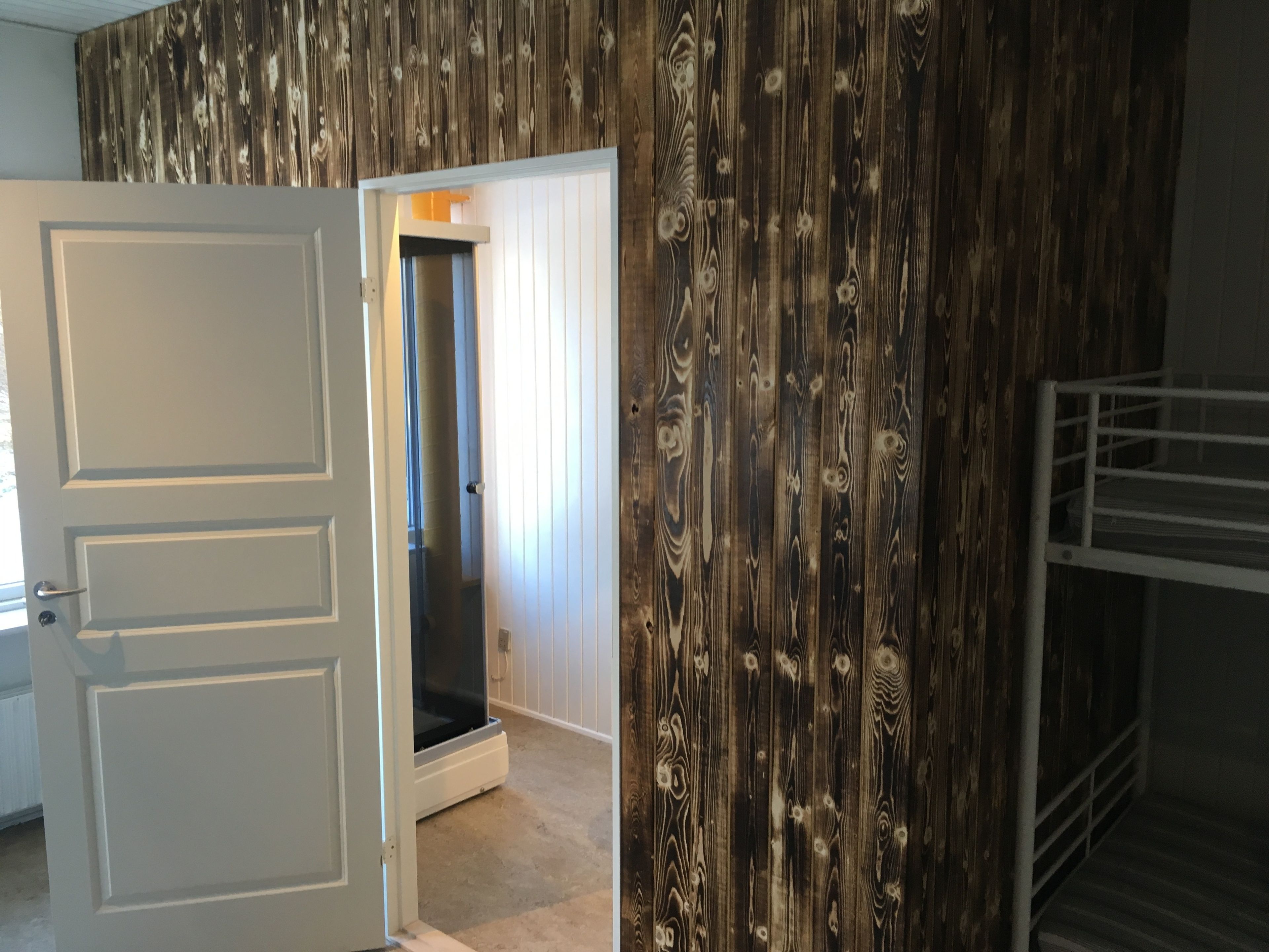 A room with a wooden wall, a white door, and a metal railing.