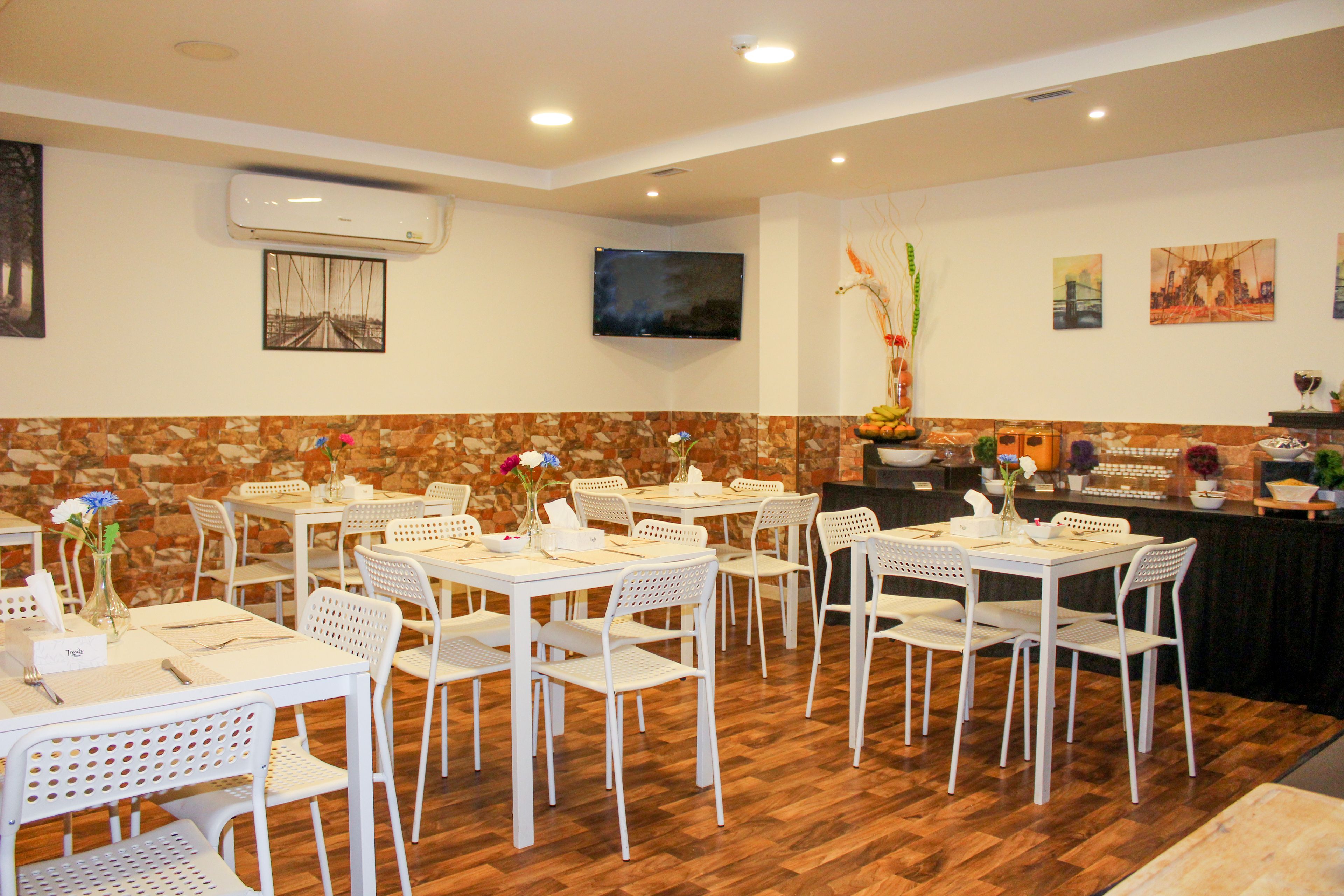 Un restaurant avec des tables et des chaises blanches, un mur en pierre et un téléviseur à écran plat fixé au mur.