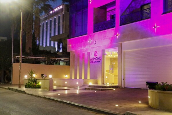 A hotel entrance with a sign for 'ALMOND HOTEL APARTMENTS' and a visible entrance door.