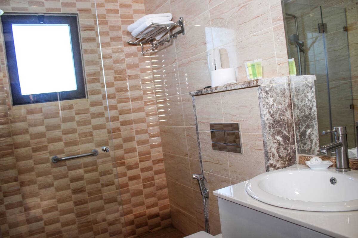 A bathroom with a checkered tile wall, a glass shower enclosure, a white sink, and a mirror with a marble frame.