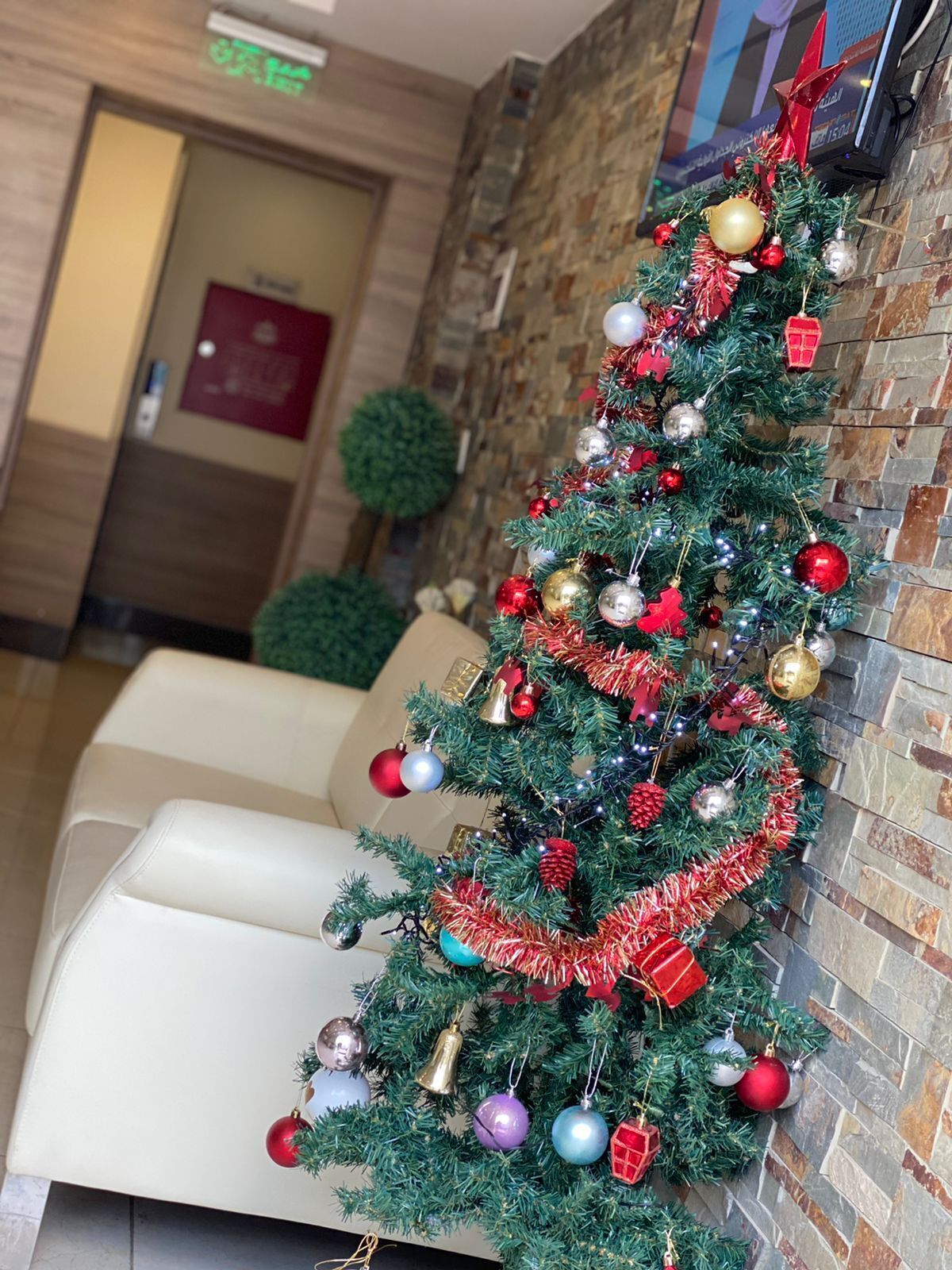 Un árbol de Navidad adornado con diversos adornos e iluminación, situado frente a una pared de piedra en la zona de recepción de un hotel.