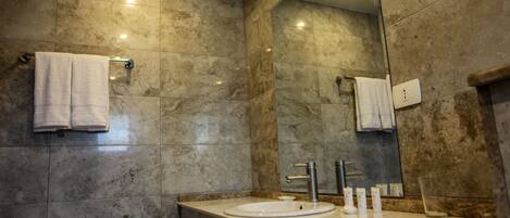 Un baño moderno con pared de azulejos de mármol, un espejo grande, un lavabo con dos grifos y un perchero para toallas.