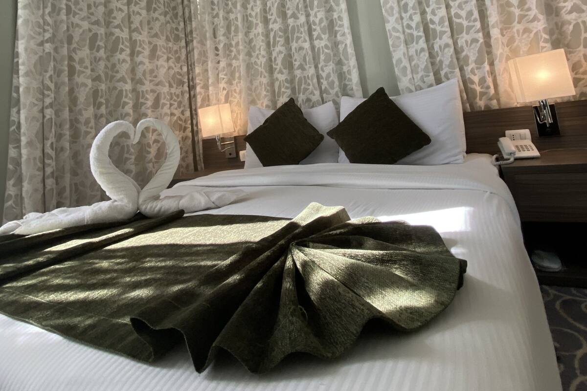 A hotel room with a neatly made bed, two bedside lamps, a telephone, and a decorative swan on the bed.
