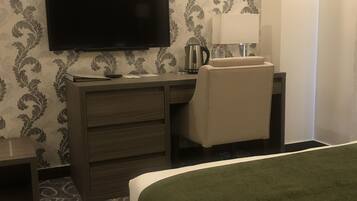 A hotel room with a bed, a desk with a flat-screen TV, a coffee maker, and a lamp.