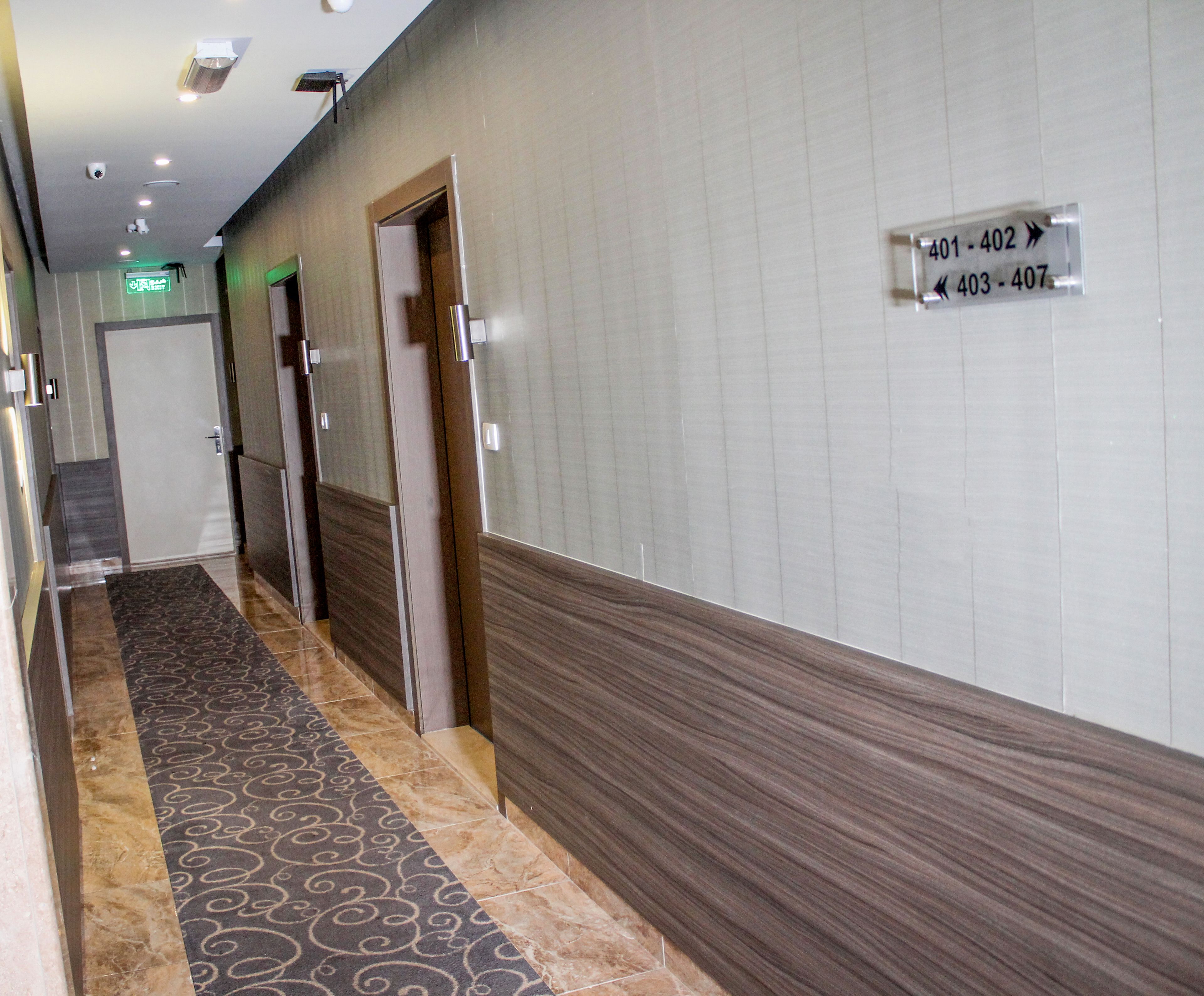 A hotel hallway with a patterned carpet, a sign indicating room numbers, and a door with a frosted glass panel.