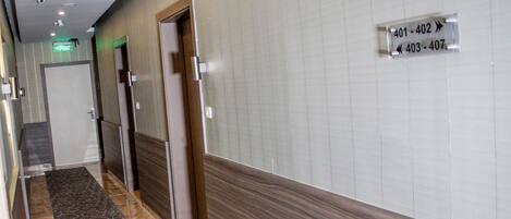 A hotel hallway with a patterned carpet, a sign indicating room numbers, and a door with a frosted glass panel.
