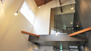 Ein modernes Interieur mit freiliegenden Holzbalken, einer Glastrennwand und einer erhöhten Galerie mit Holzgeländer.