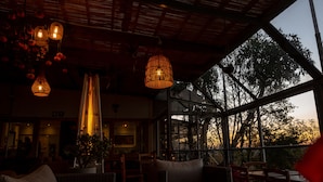 A cozy interior with wicker furniture, hanging lights, and a large window offering a view of trees.