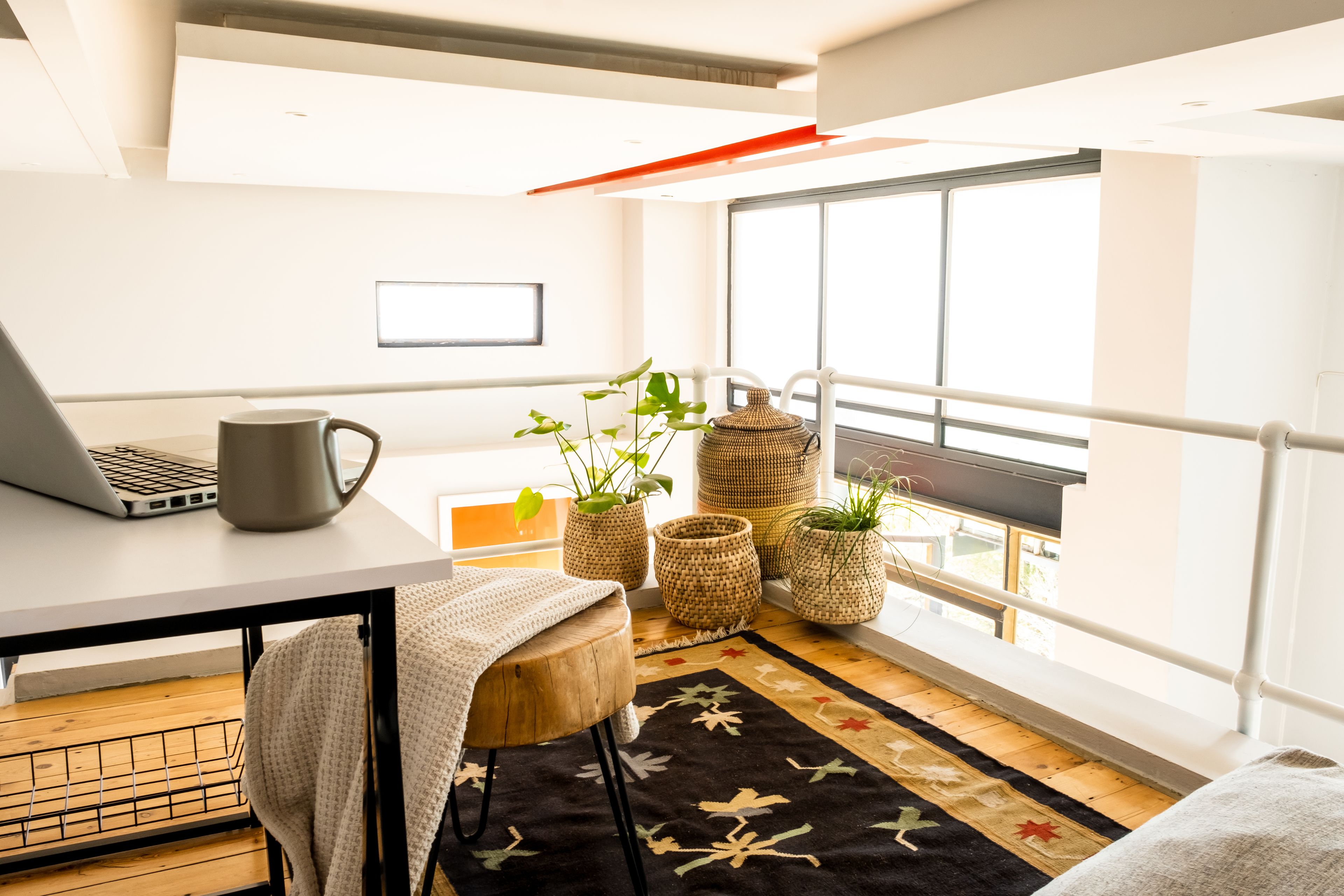 A modern, well-lit balcony with a laptop, a mug, and potted plants.