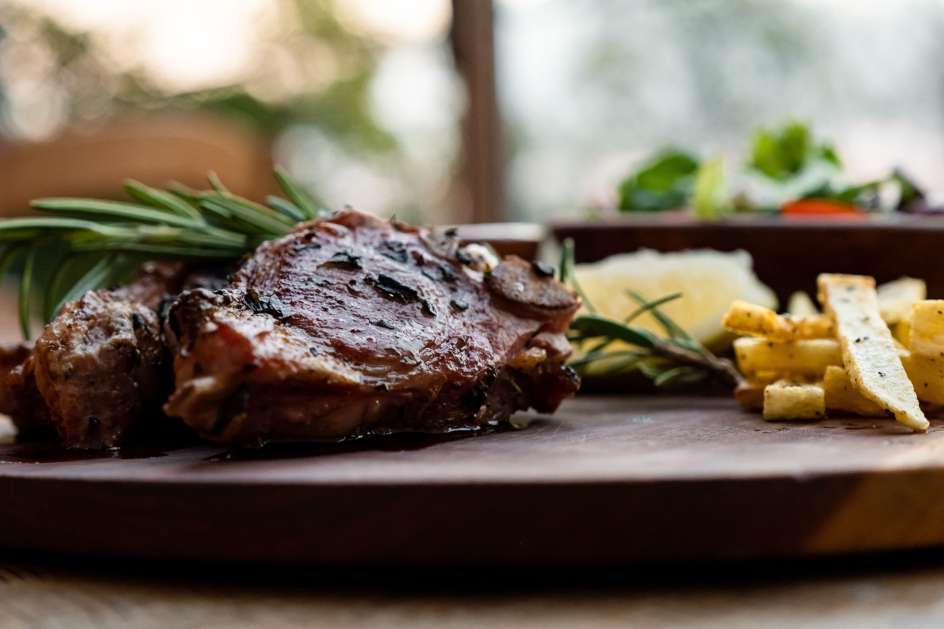 A plate with a grilled steak, rosemary, and potato wedges.