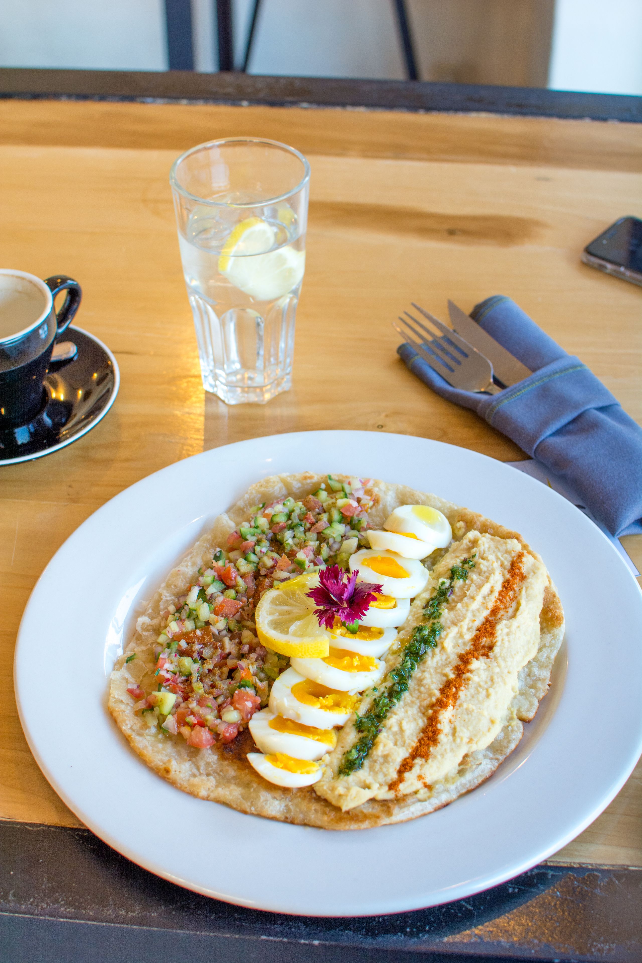 Un plato de comida con huevos, vegetales verdes y una rodaja de limón sobre un plato blanco.