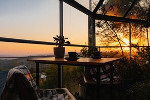 A table with a potted plant, two cups, and a plaid blanket in a room with large windows overlooking a landscape. - Pablo House (Johannesburg)