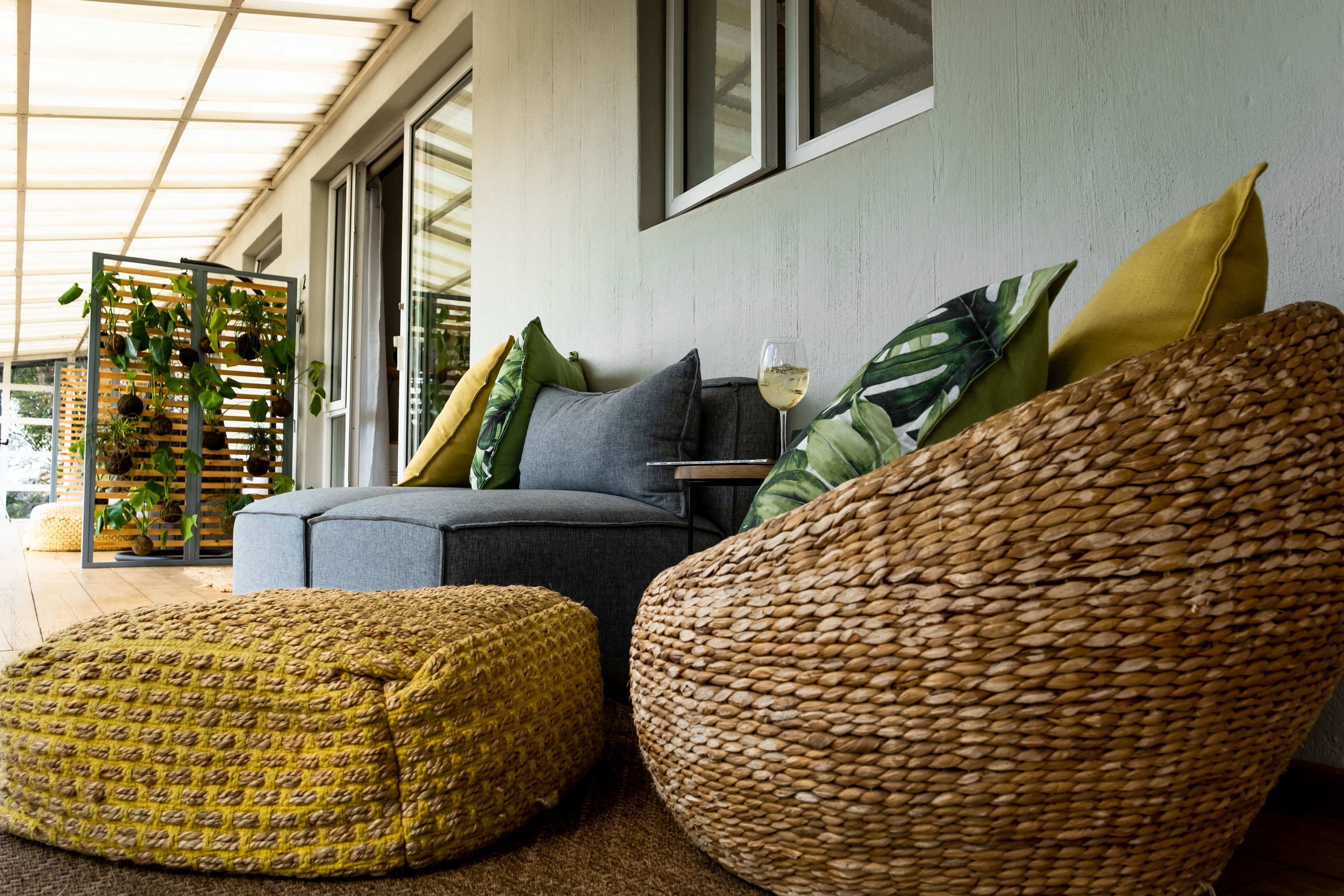 Un salon moderne avec un canapé gris, des coussins jaunes et verts, un fauteuil en osier et un pouf tressé.