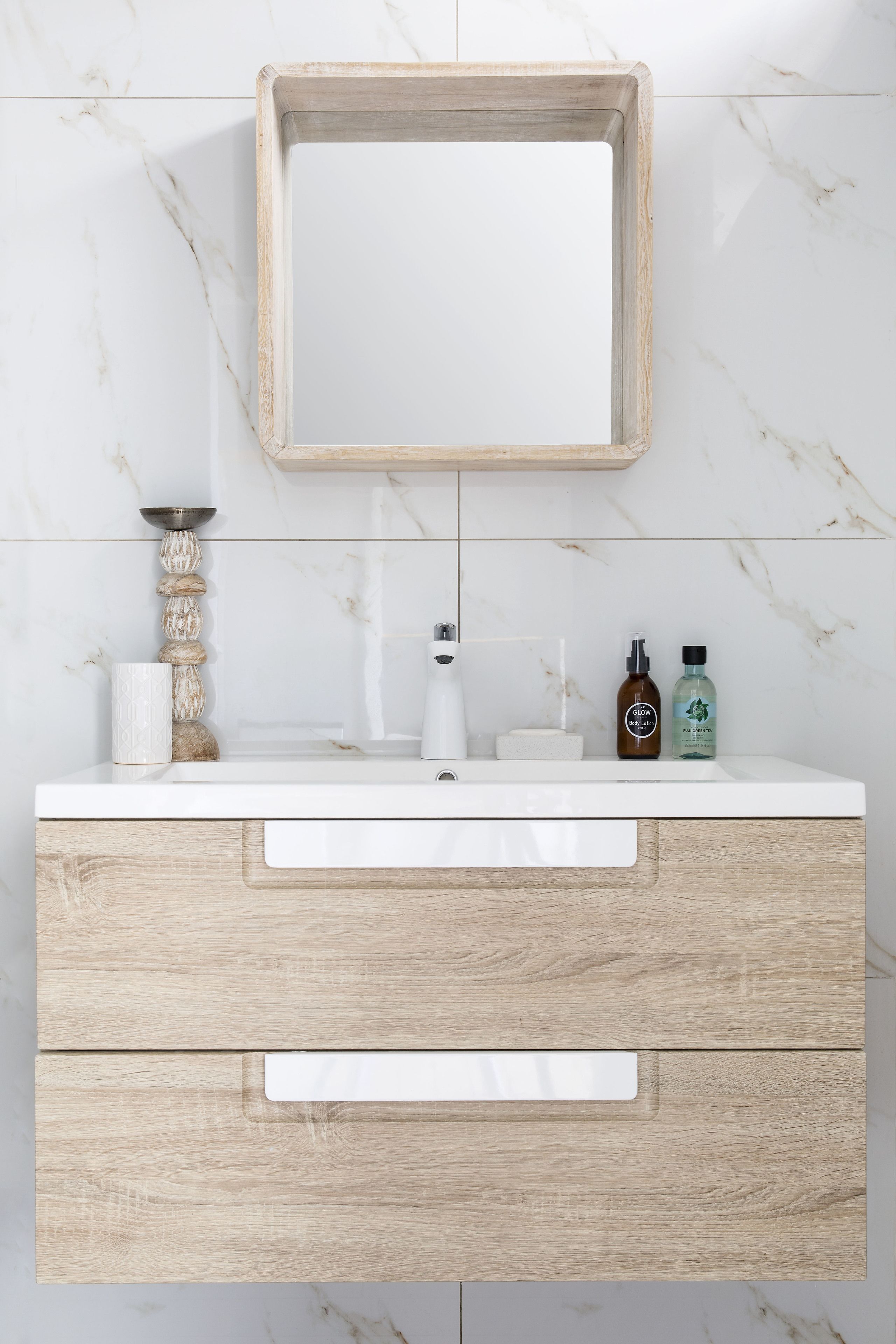 A bathroom vanity with a marble backsplash, a wooden frame mirror, and a white countertop.