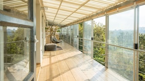 A modern hotel suite with a large glass balcony, wooden flooring, and a view of the surrounding forest.