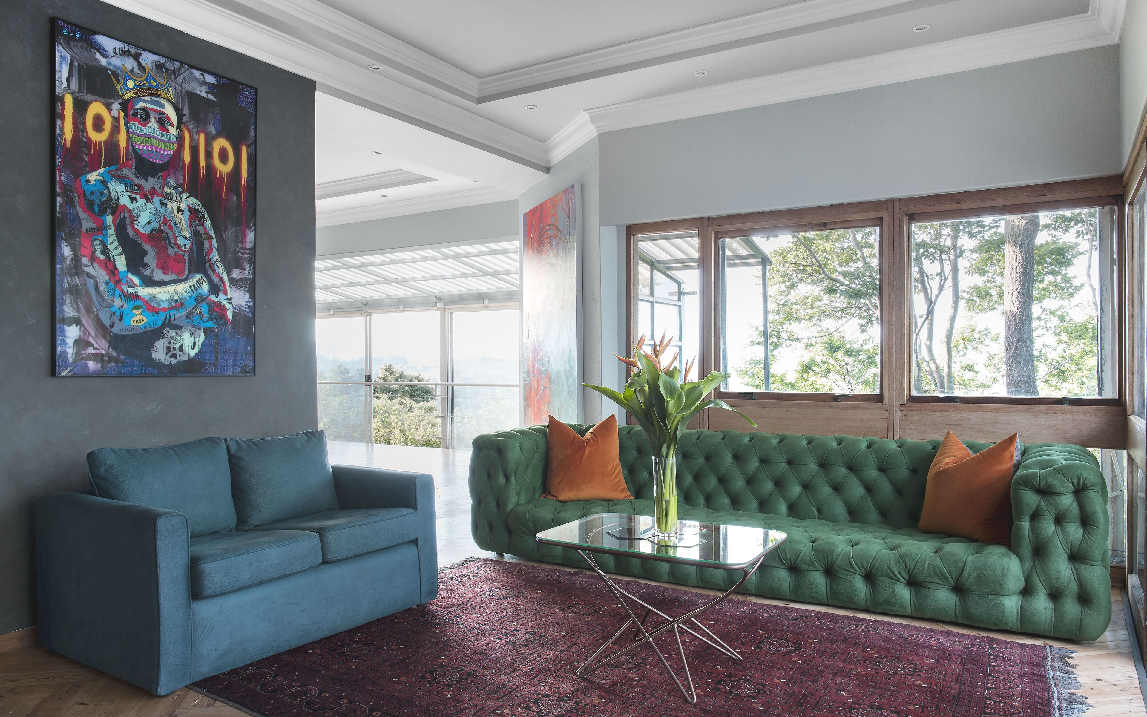 A modern living room with a green sofa, blue armchair, and a glass coffee table.