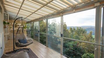 A modern balcony with a hanging chair, a cushioned bench, and a view of a forested landscape.