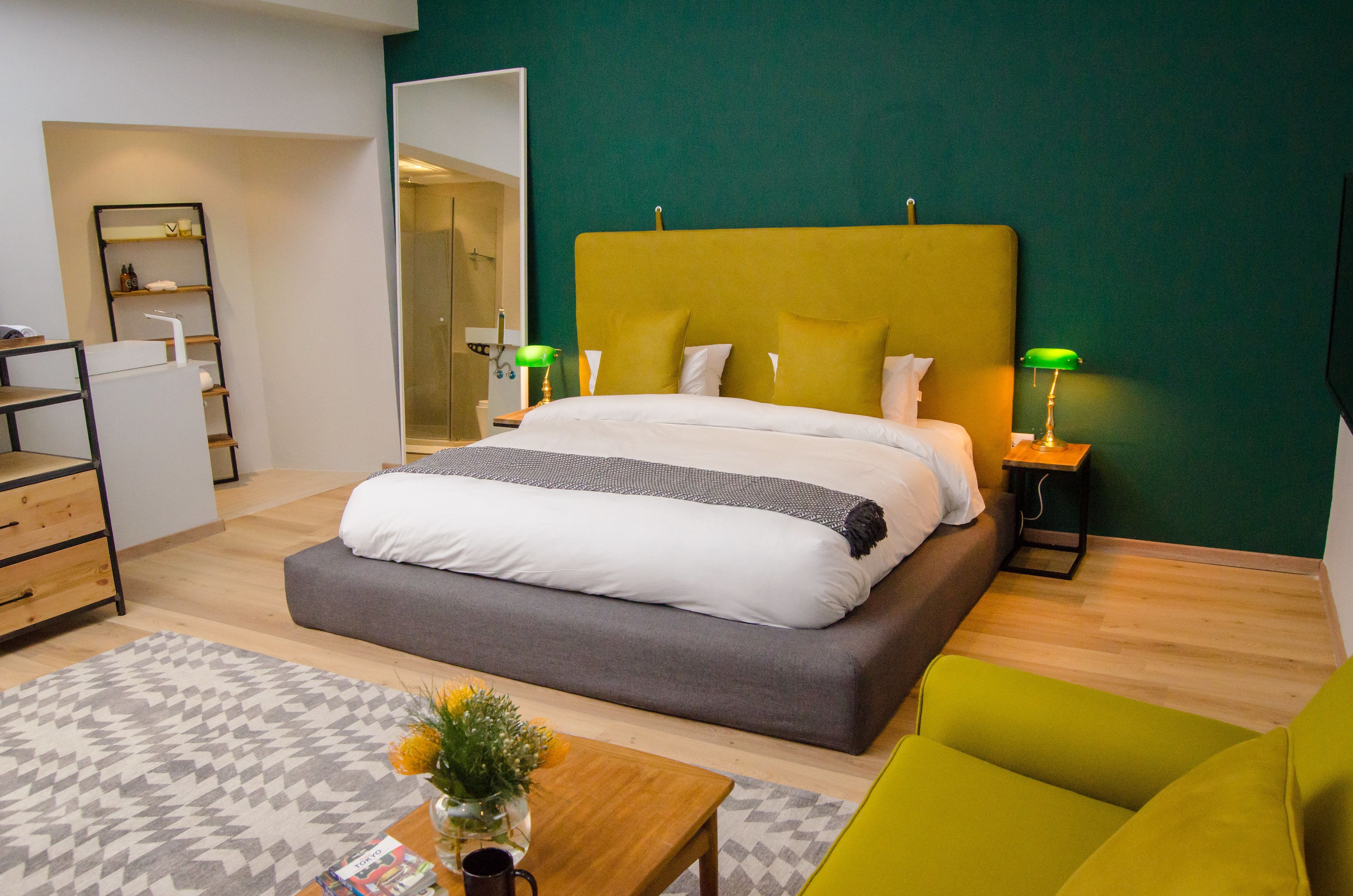 Un dormitorio moderno con una cama grande, lámparas de noche, un aparador de madera y un sillón verde.