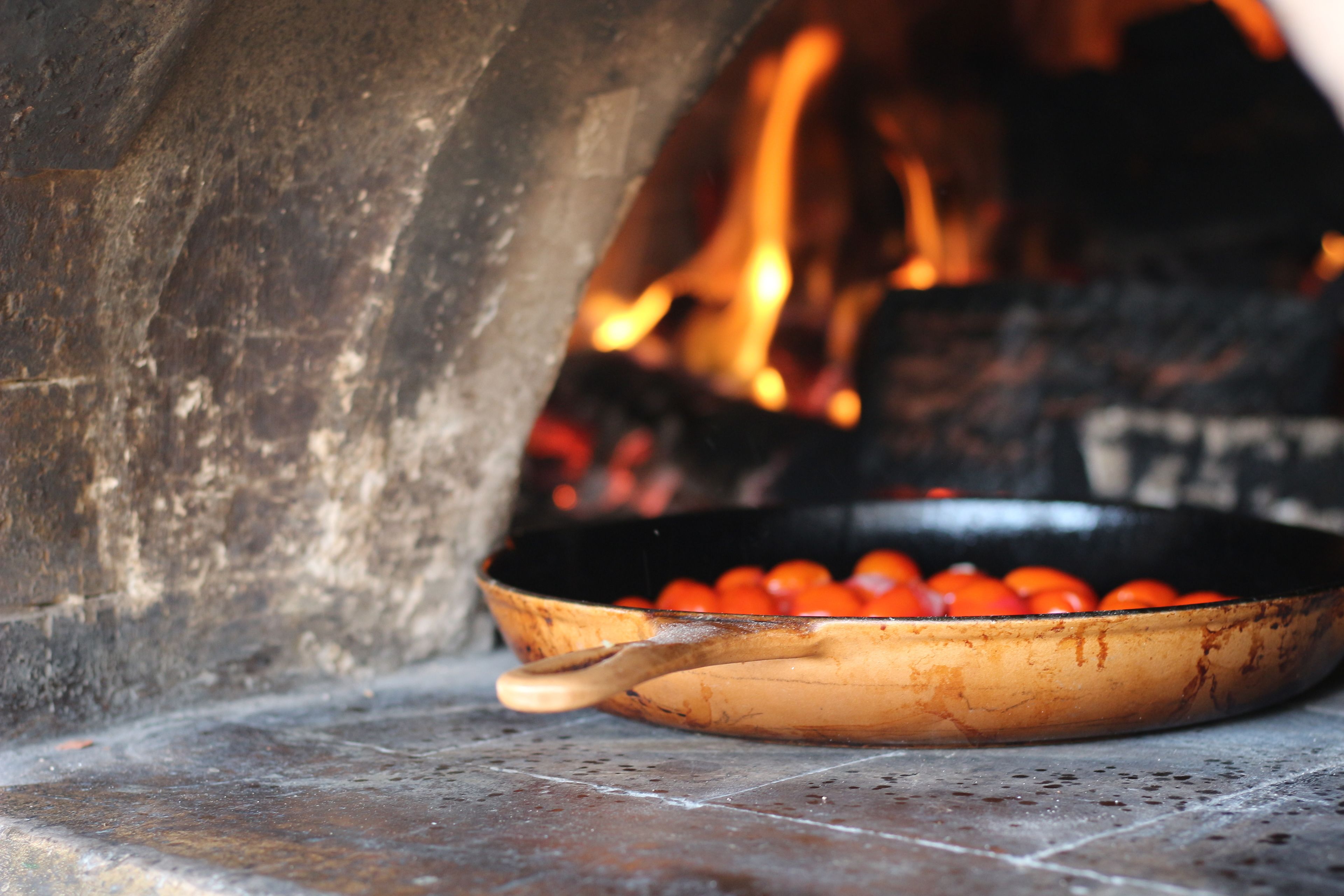 Een stenen oven met een houten pan vol tomaten.