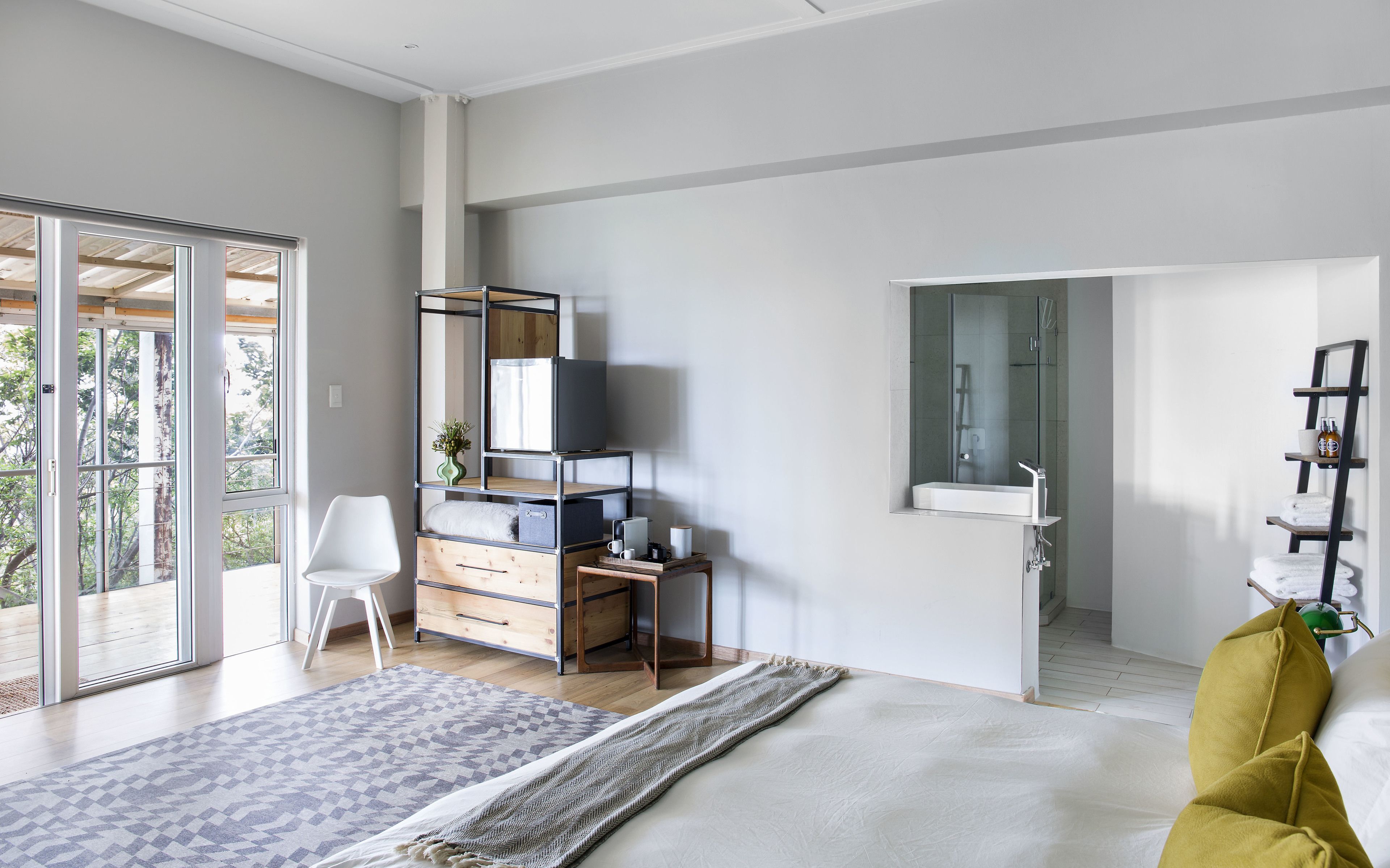 Quarto moderno com cama grande, escrivaninha, cadeira, guarda-roupa, televisão e banheiro com espelho e pia.