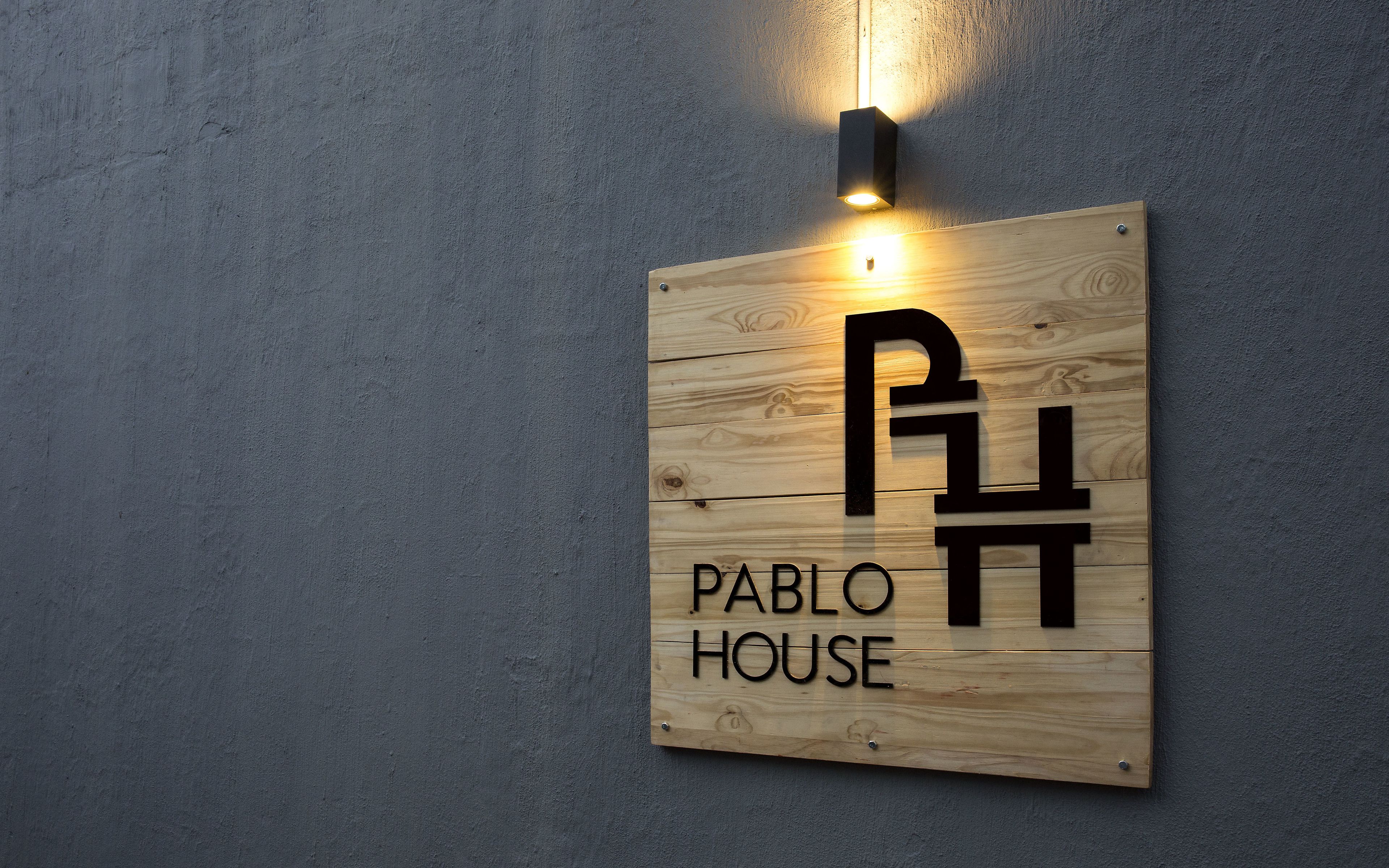 Un letrero de madera con la inscripción 'Pablo House', sujeto a una pared con textura.