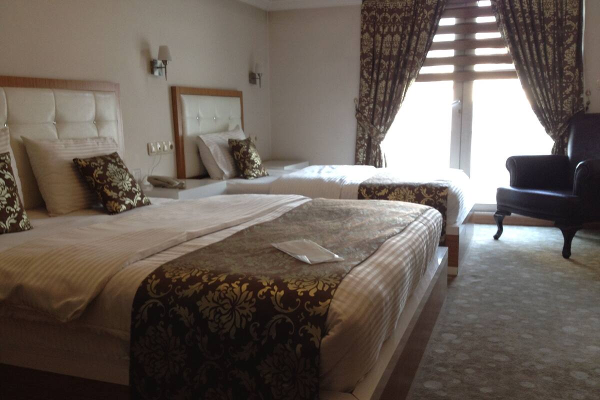 Une chambre d’hôtel avec deux lits, une chaise et une fenêtre avec des rideaux.