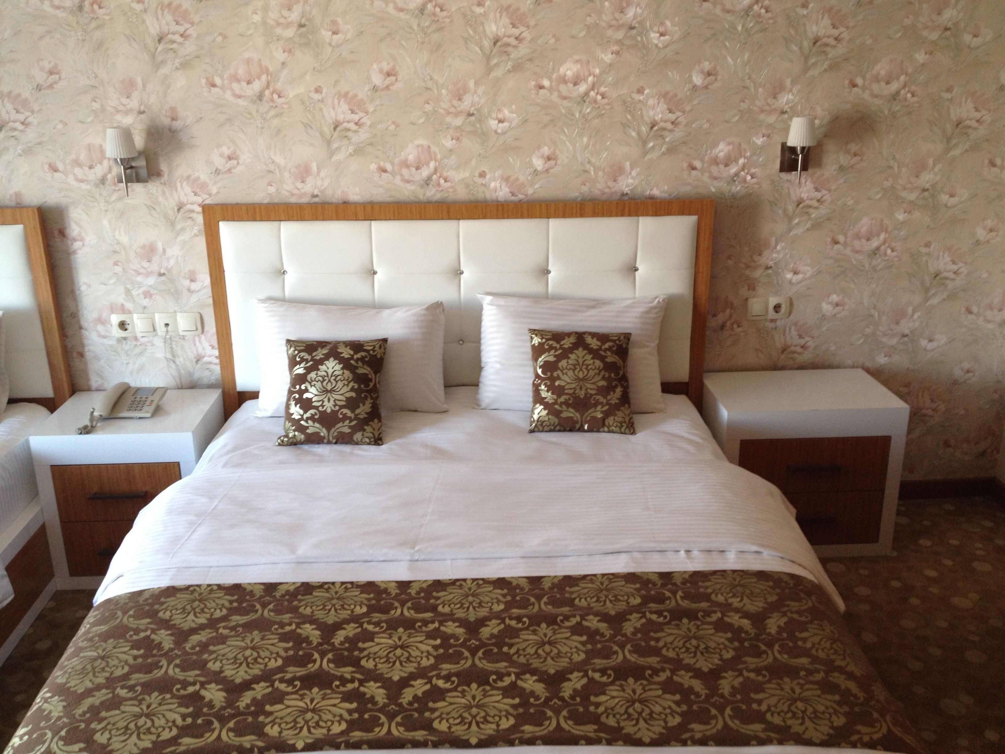 Quarto de hotel com uma cama grande, duas mesas de cabeceira, um telefone e papel de parede floral.