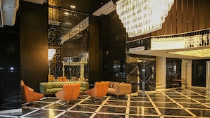 Un vestíbulo con piso de mármol a cuadros, asientos modernos, una escalera y un candelabro.