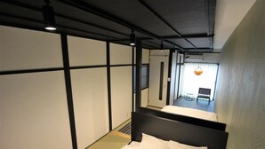 A hotel room with tatami flooring, a black headboard, and a bed with white bedding. - SEKAI HOTEL Tsuki (Osaka)