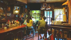 A bar with wooden furniture, a counter with various bottles, and a large window with a view of greenery. - SEKAI HOTEL Tsuki (Osaka)