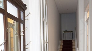 A hallway with a wooden coat rack, a staircase with a red carpet, and patterned floor tiles. - Casa Velha Guesthouse (Porto)