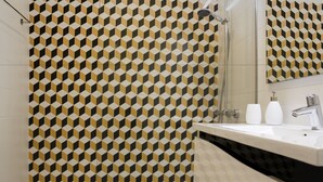 A bathroom with a geometric patterned tile wall, a white sink with a black countertop, and a mirror above the sink. - Casa Velha Guesthouse (Porto)