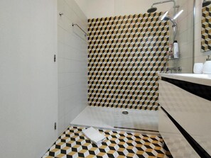 A modern bathroom with a geometric patterned tile design, a shower area, and a vanity with a mirror. - Casa Velha Guesthouse (Porto)