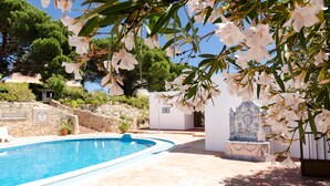 A swimming pool with a stone pathway, a small building, and a decorative fountain. - Bem Parece (Albufeira)