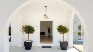 Un espace d’accueil agrémenté d’une arche blanche, de deux arbres en pot, d’un luminaire moderne et d’un comptoir de réception.