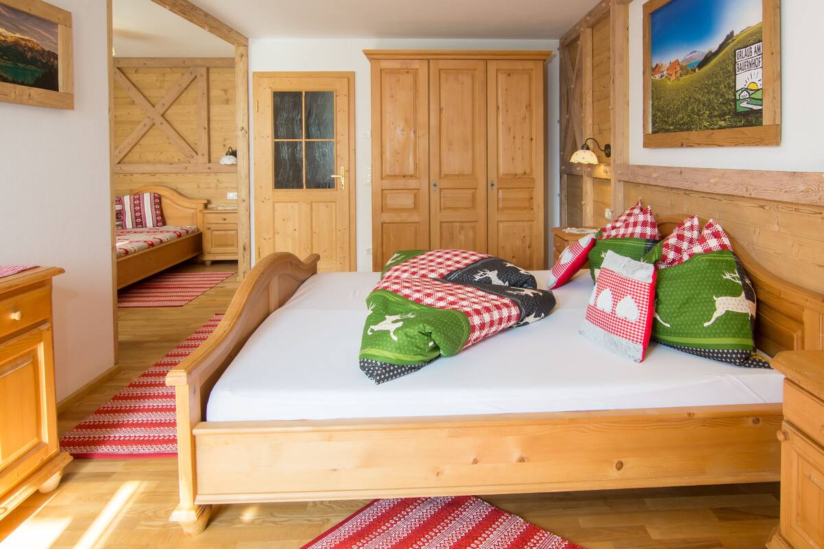 Una cama de madera con una colcha a cuadros rojo y blanco y almohadas verdes, un armario de madera y suelo de madera.