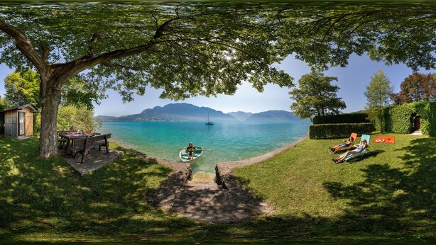 Uitzicht op een meer met een boot, een picknicktafel en twee mensen die ontspannen op ligstoelen.