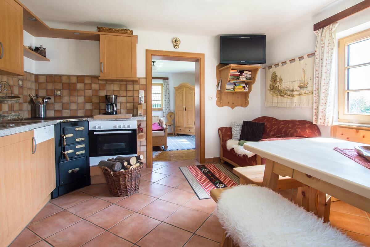 Una cocina con armarios de madera, estufa y comedor con mesa y sofá.