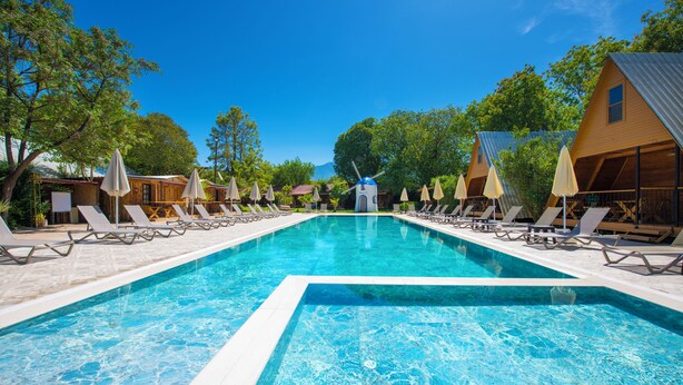 Una piscina con sillas de descanso y sombrillas, rodeada de cabañas de madera.
