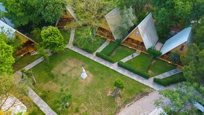 Vista aérea de un resort con varias cabañas, un área central con césped y un camino pavimentado.