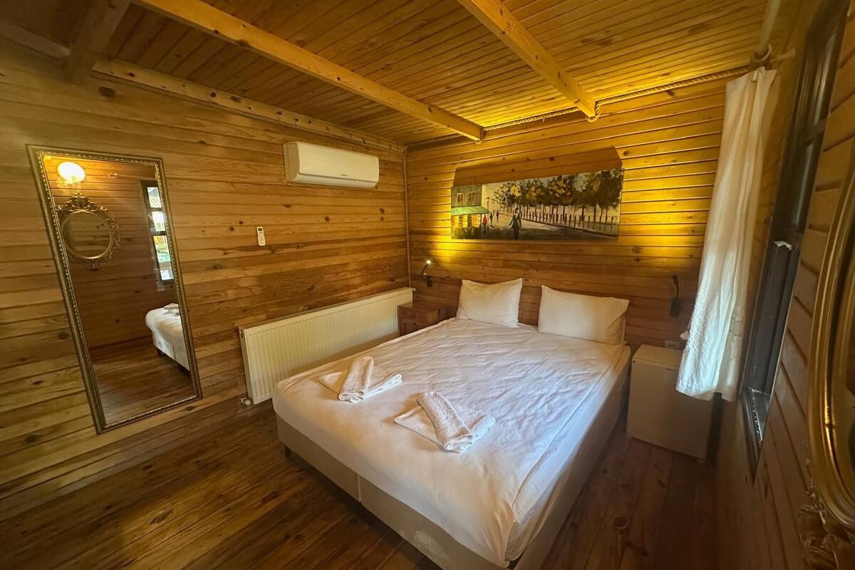 Une chambre dans une cabane en bois, avec un lit, un miroir, un climatiseur et un tableau accroché au mur.