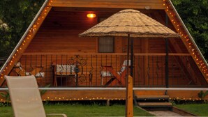 Una cabaña de madera con techo triangular, luces colgantes, un porche cubierto y una silla de descanso.